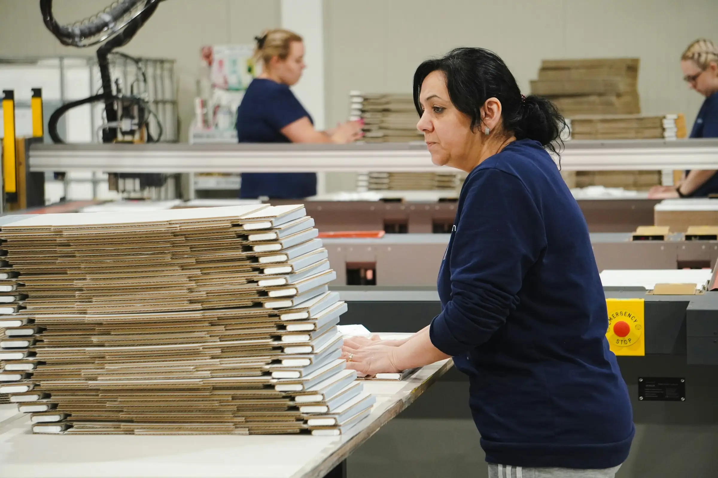 Worker at a packaging converting line stacking flat corrugated blanks