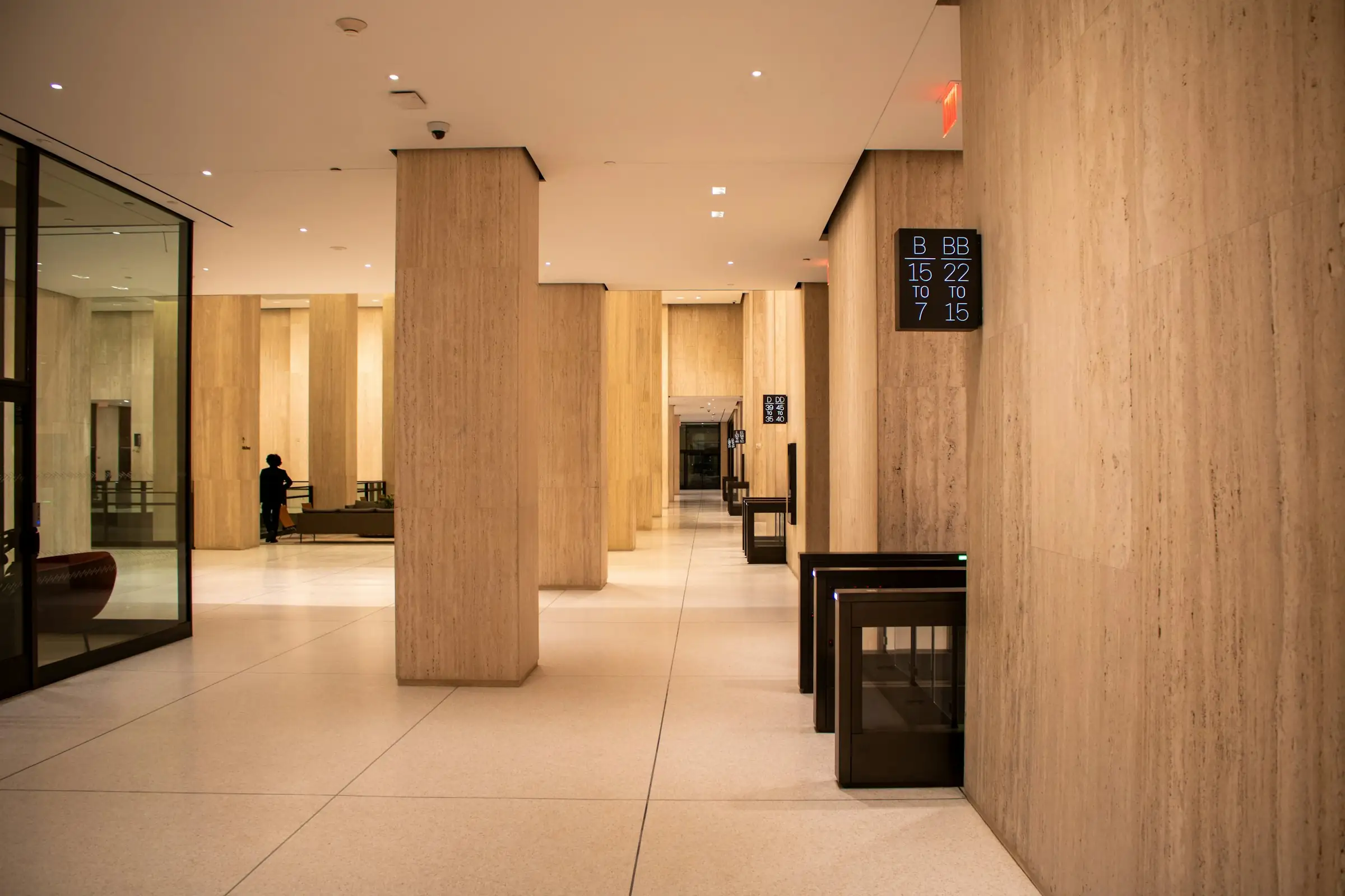 Travertine-clad lobby of a commercial office tower with elevator bank and security desks