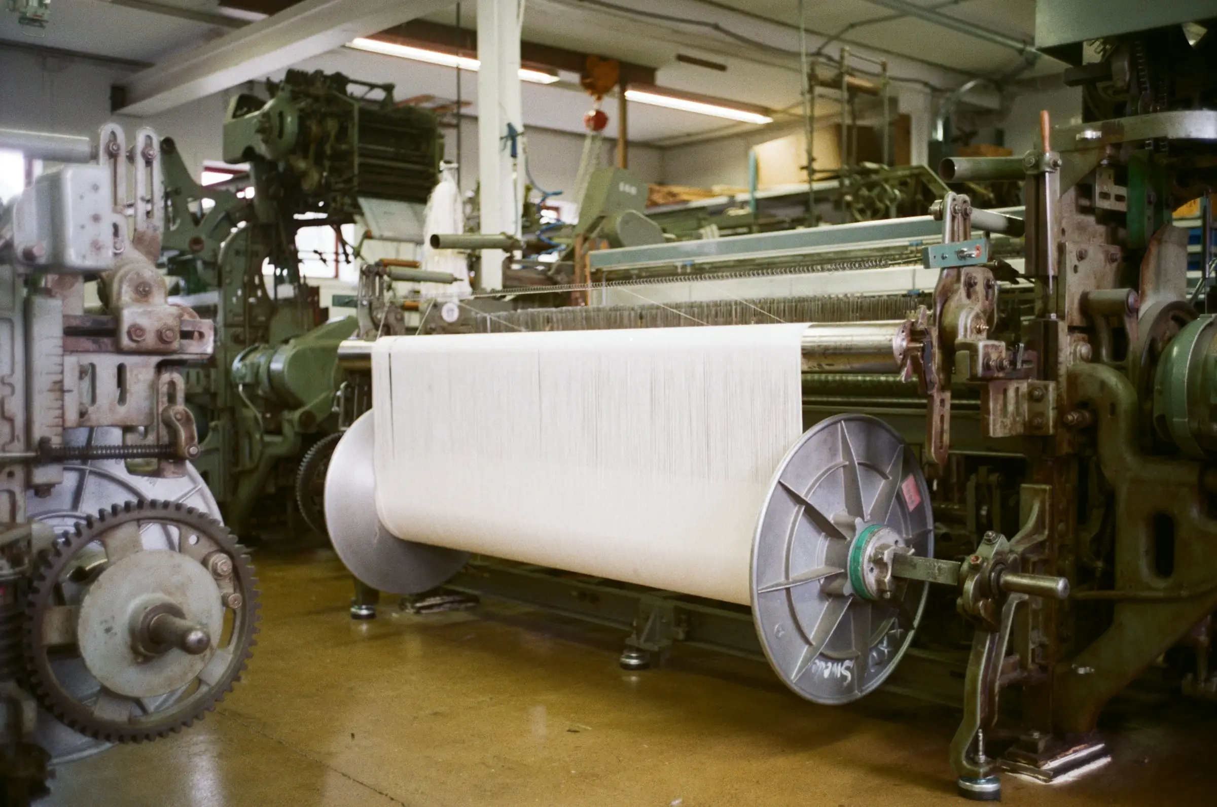 Industrial weaving loom with a large roll of white fabric